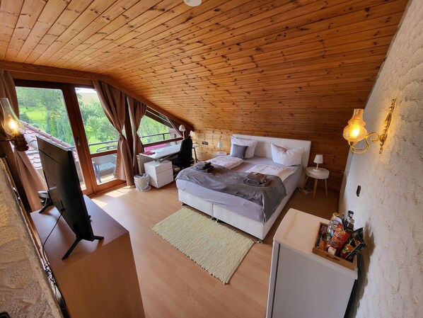 A bedroom with a wooden ceiling, a bed with pillows, a desk with a chair, a small table, and a nightstand.