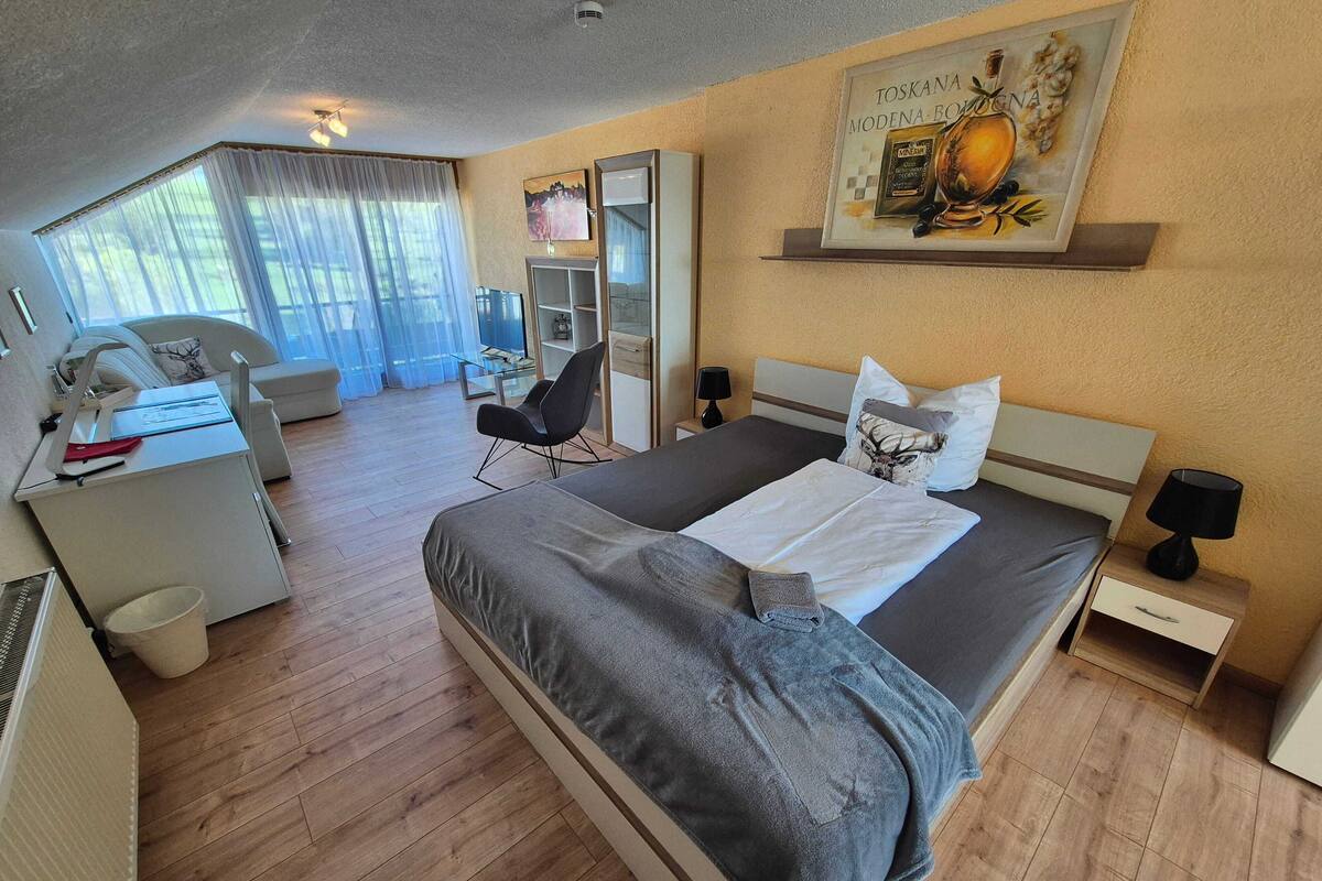 Ein Hotelzimmer mit Bett, Nachttischen, Schreibtisch, Stuhl, Spiegel und einem fenster mit Vorhängen.