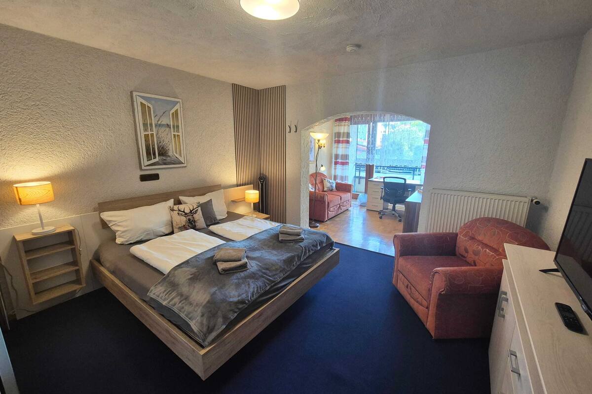 Ein Schlafzimmer mit einem Bett, Nachttischen, einem Schreibtisch, einem Stuhl und einem Fernseher.