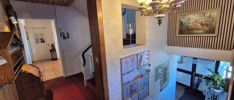 A wooden interior with a chandelier, a staircase, and a bulletin board with notices.
