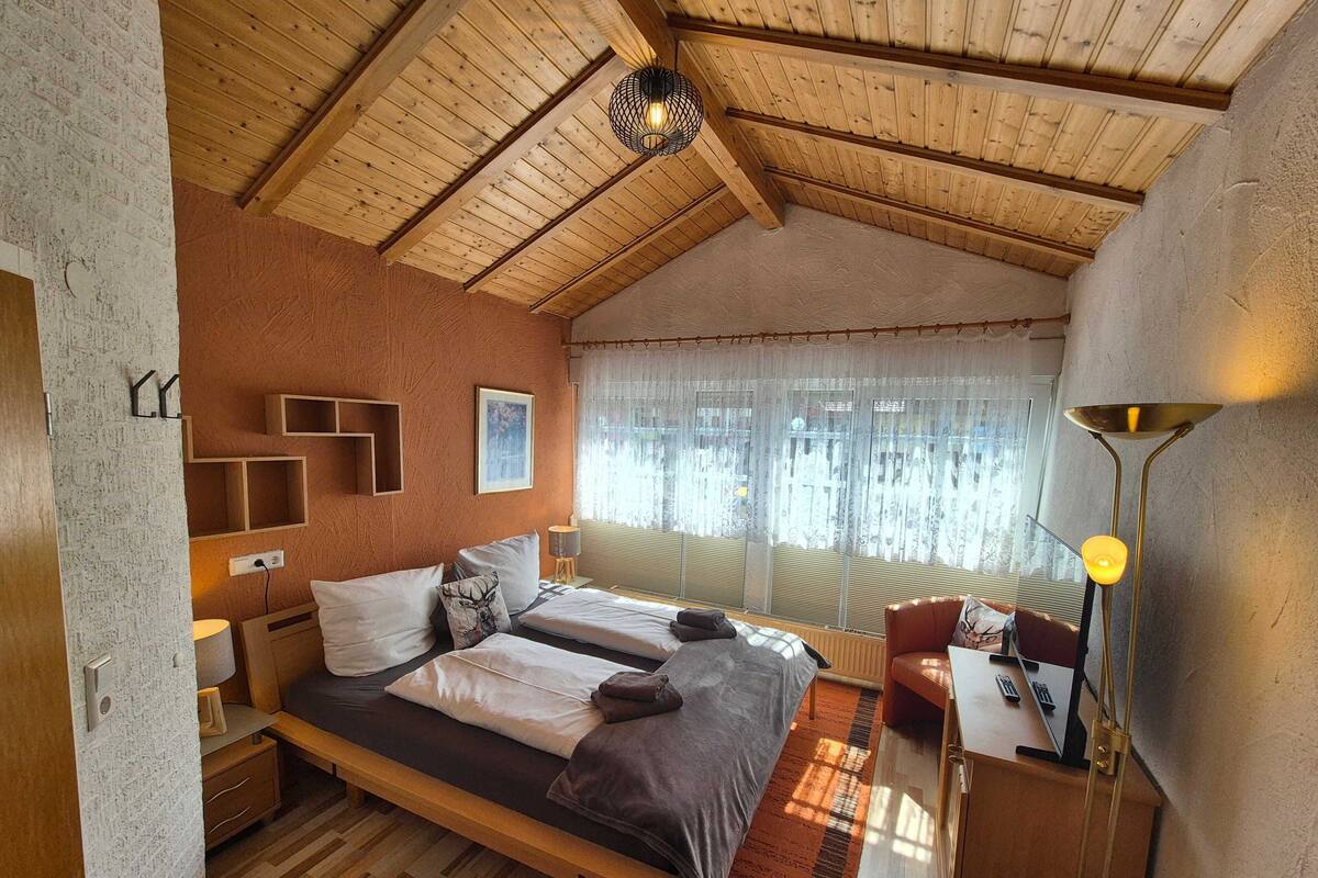Ein Schlafzimmer mit zwei Betten, einem Schreibtisch, einem Stuhl, einer Lampe und einem Fenster mit Vorhängen.