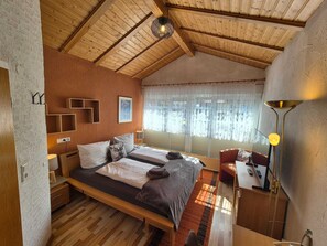 Ein Schlafzimmer mit zwei Betten, einem Schreibtisch, einem Stuhl, einer Lampe und einem Fenster mit Vorhängen.