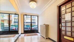 Hotellin aula, jossa on suuret ikkunat, koristeellinen kattokruunu ja puinen ovi.
