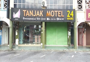 A Tanjak Motel with a 24-hour service sign, a website URL, and contact numbers.