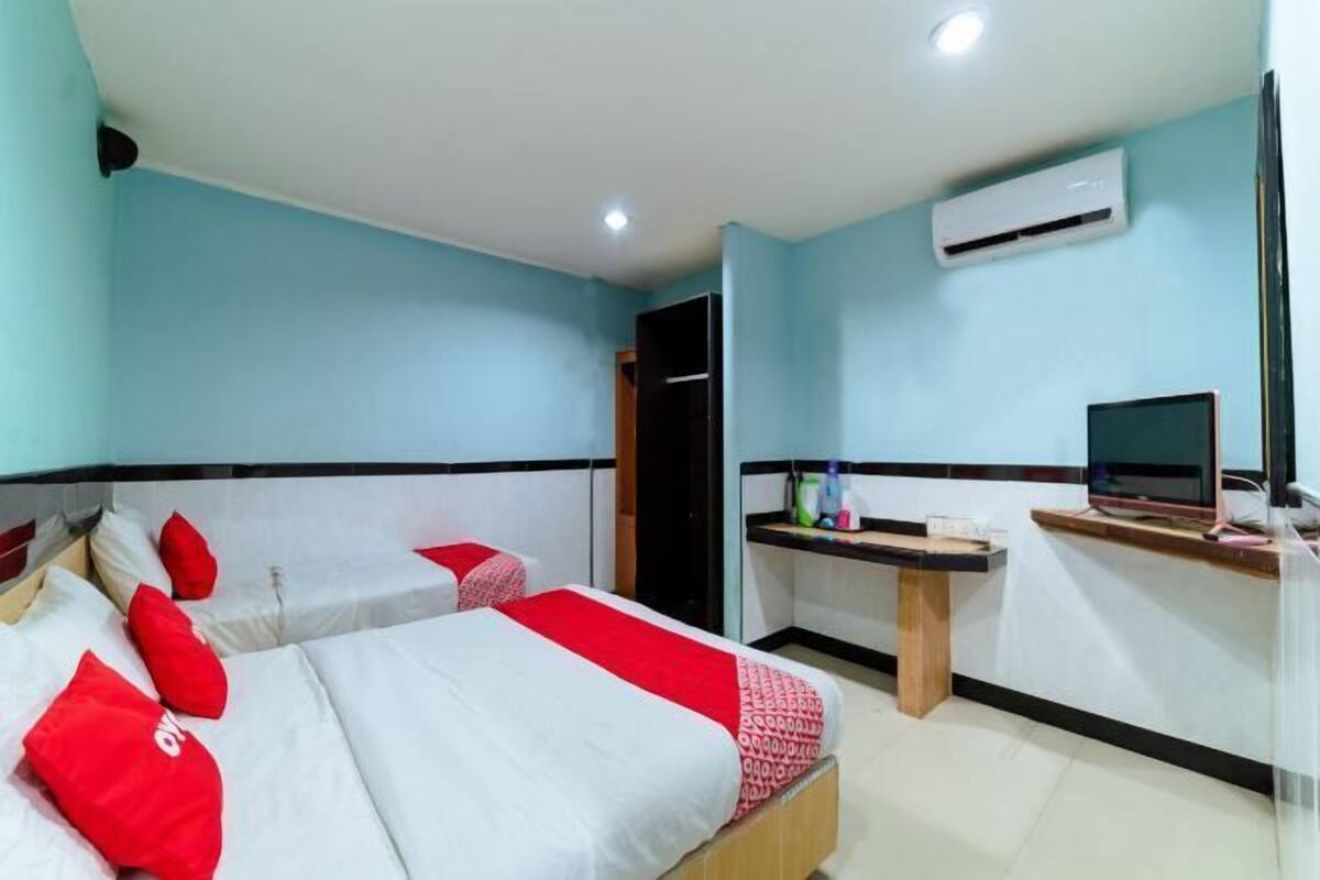 A hotel room with two beds, a desk, an air conditioner, and a TV.