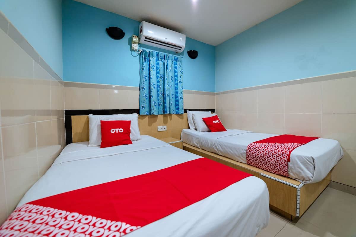 A hotel room with two beds, each with white bedding and red accents, a blue wall, and an air conditioning unit.
