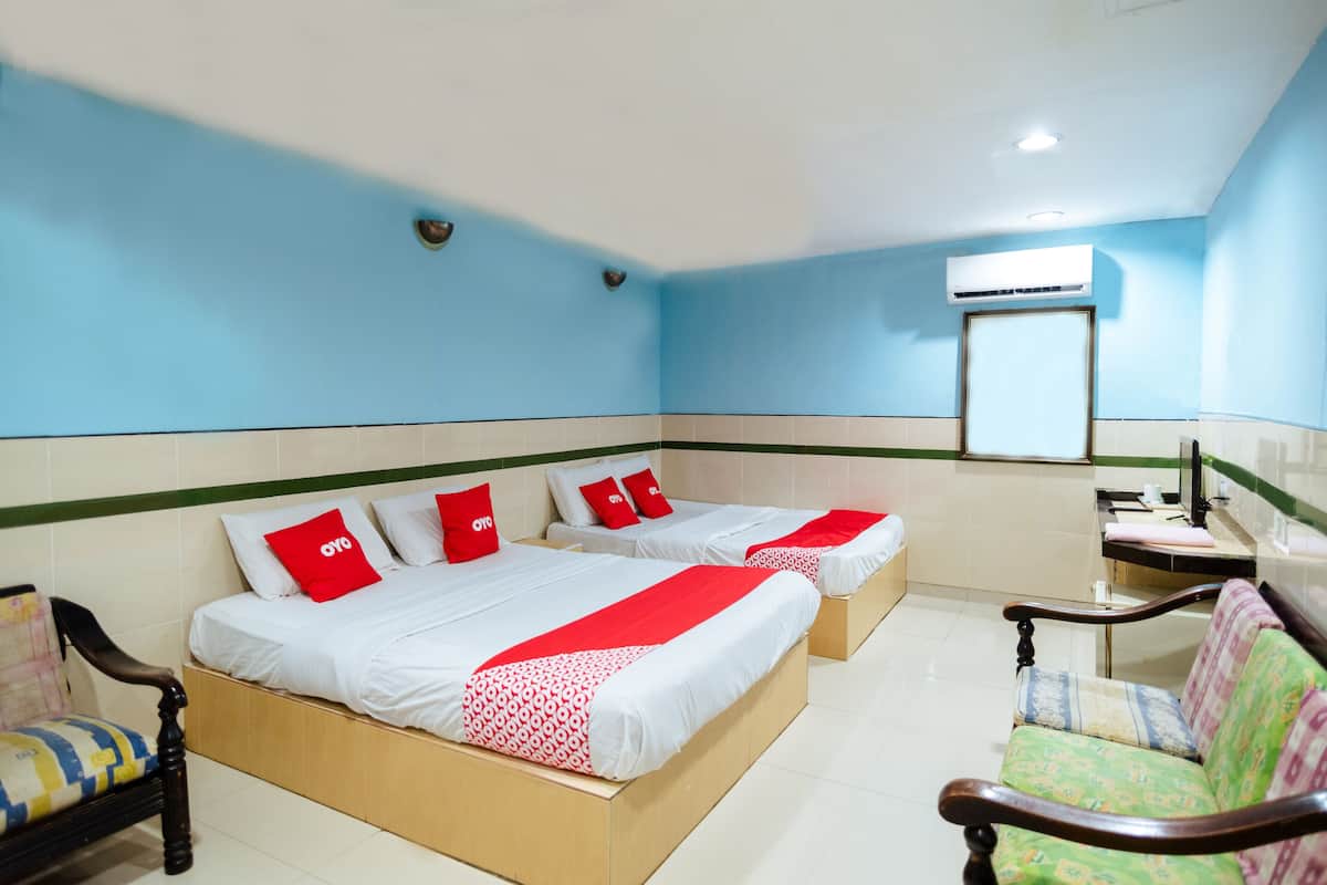 A hotel room with two beds, a chair, a small table, and an air conditioning unit.