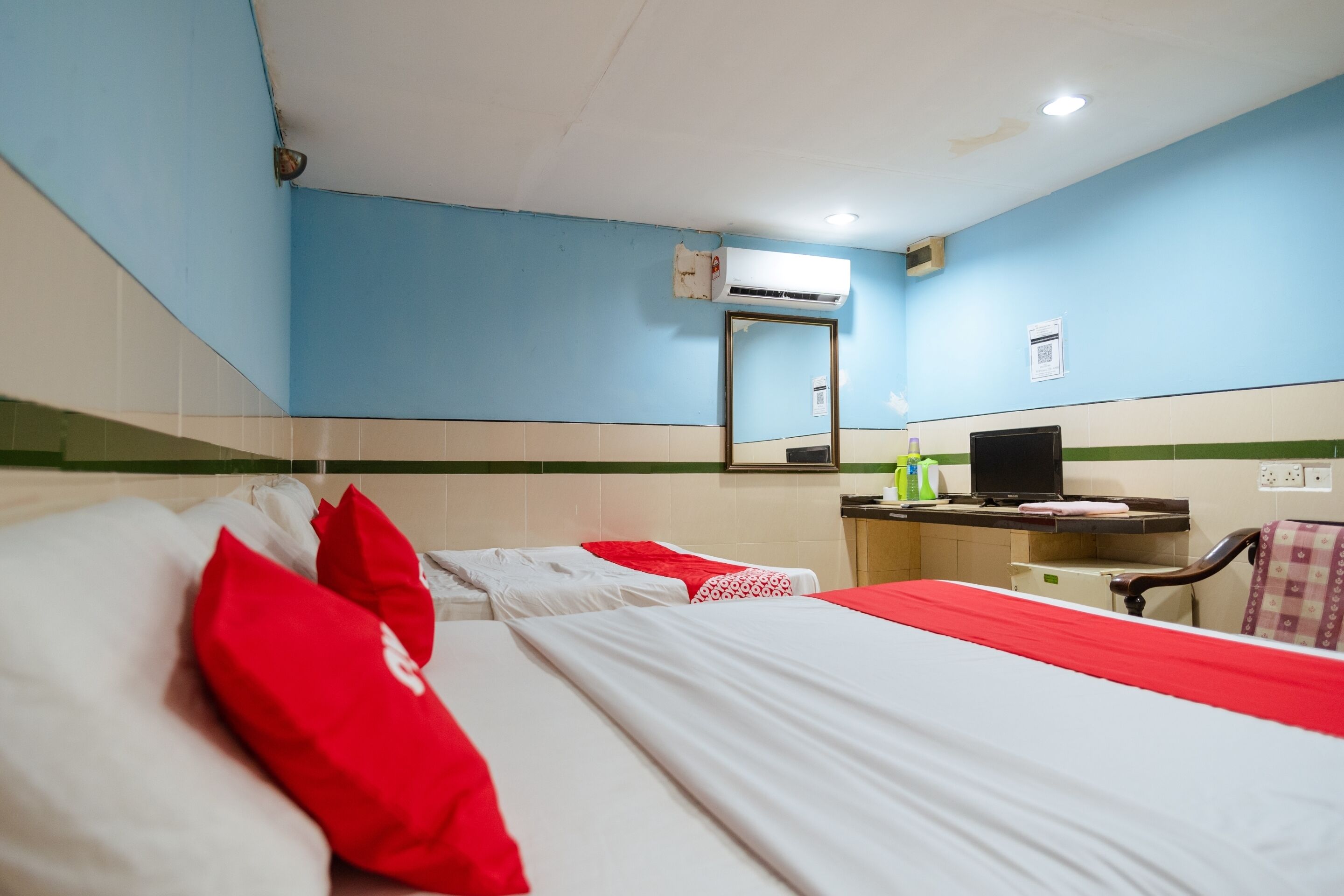 Une chambre d’hôtel avec deux lits, un bureau avec un ordinateur, un appareil de climatisation et un miroir au mur.