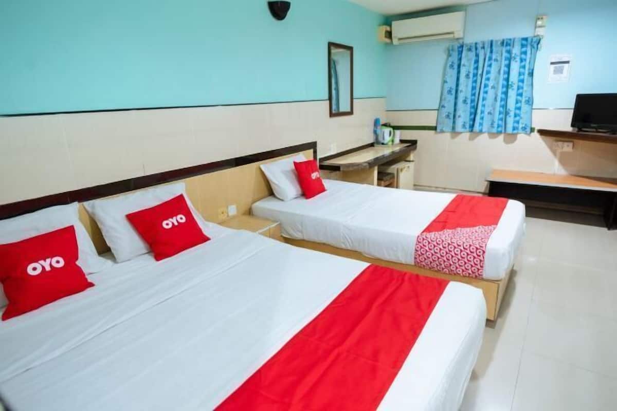Two single beds with red and white bedding, a small desk, and a television in a hotel room.