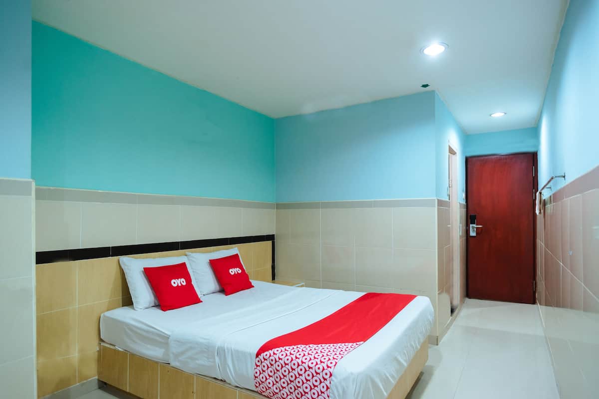 A hotel room with a bed, a red and white patterned blanket, and a red pillow with the logo "oyo".