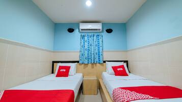 Habitación de hotel con dos camas, cada una con cubrecama rojo y blanco, y un taburete de madera pequeño entre ellas.
