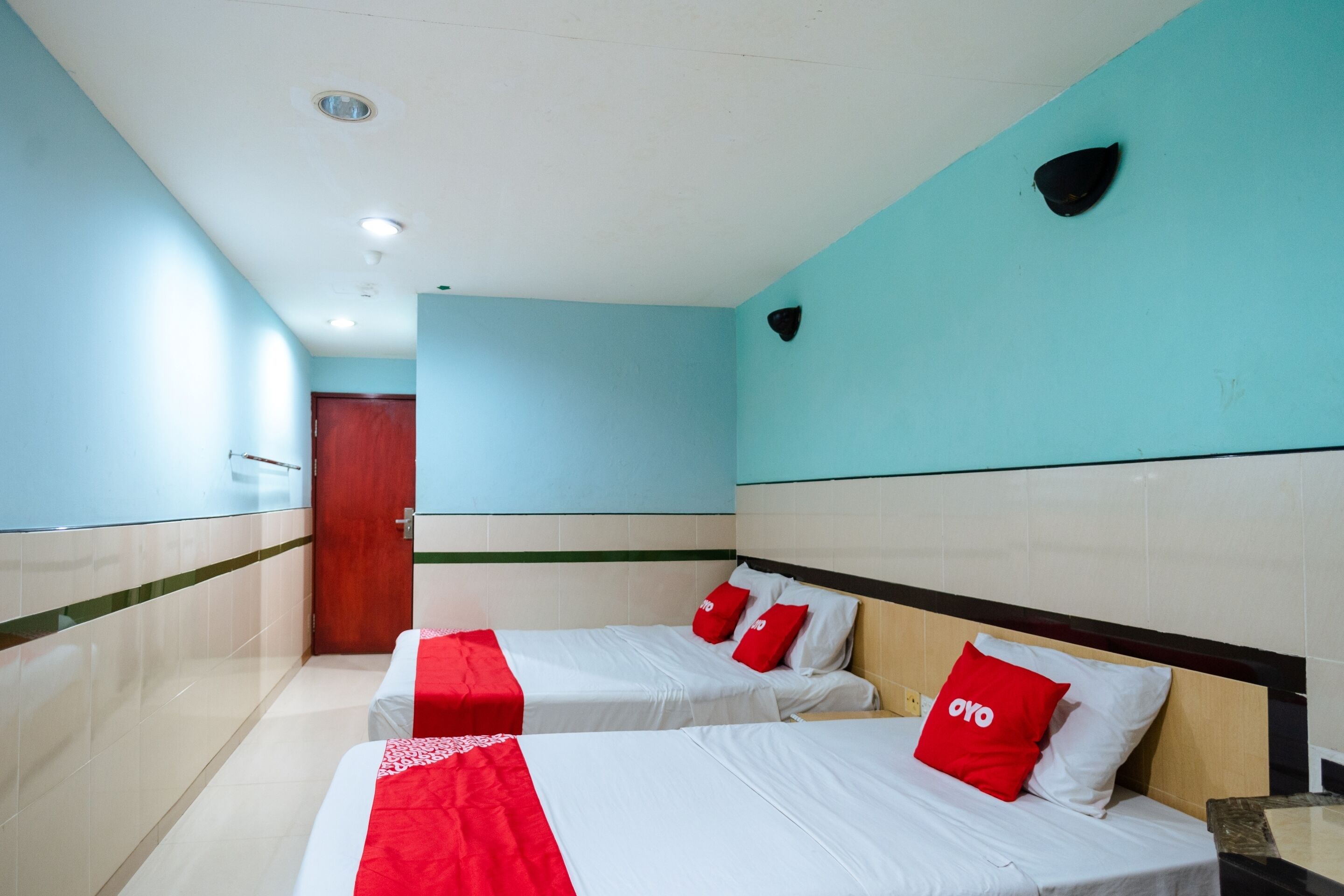 A hotel room with two beds, each with white bedding and red pillows, a wooden headboard, and a tiled floor.