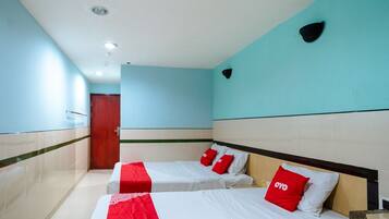 Habitación de hotel con dos camas, cada una con ropa de cama blanca y almohadas rojas, cabeceros de madera y suelo de baldosas.