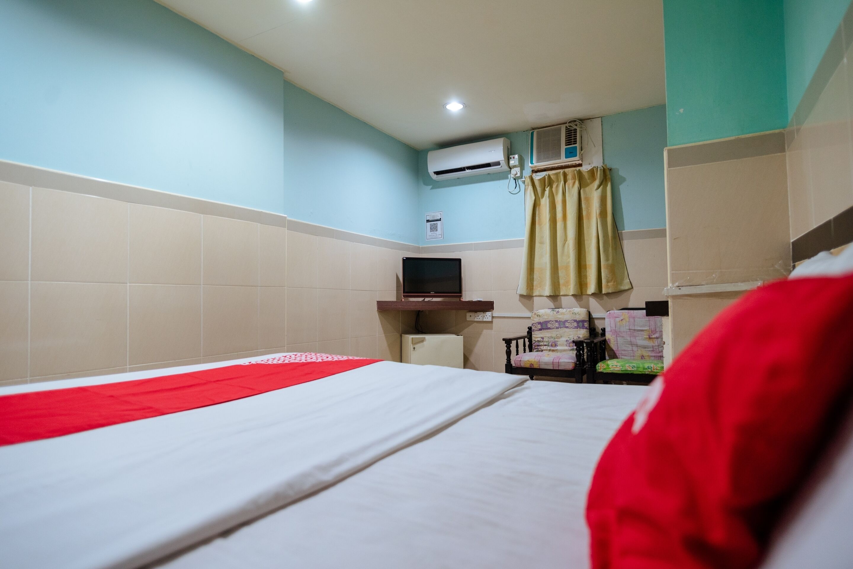 Habitación de hotel con cama, televisión, aire acondicionado y un pequeño escritorio con lámpara.