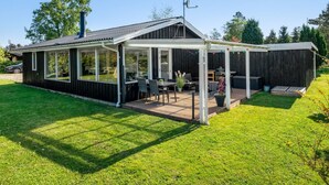 Una casa moderna con un porche cubierto, zona de barbacoa y un amplio salón con ventanales.