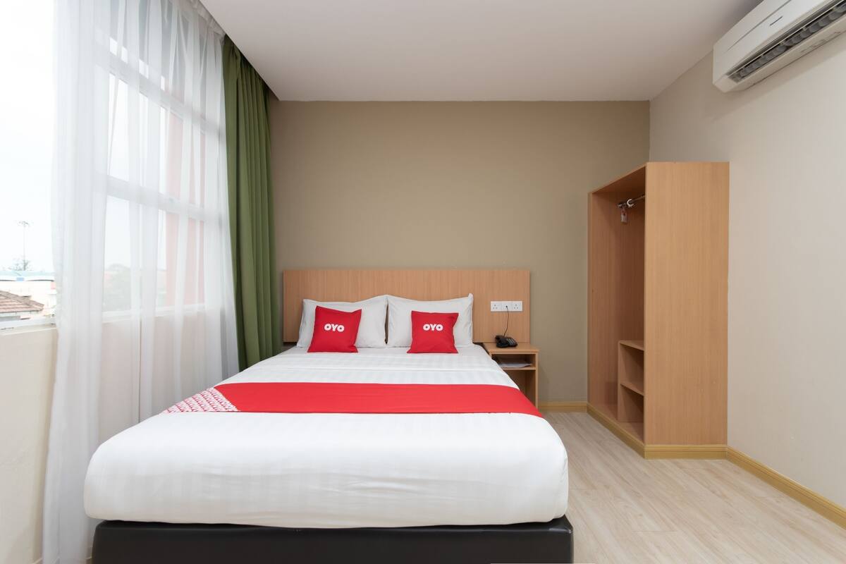 A hotel room with a bed, a nightstand, a wardrobe, and a window with curtains.