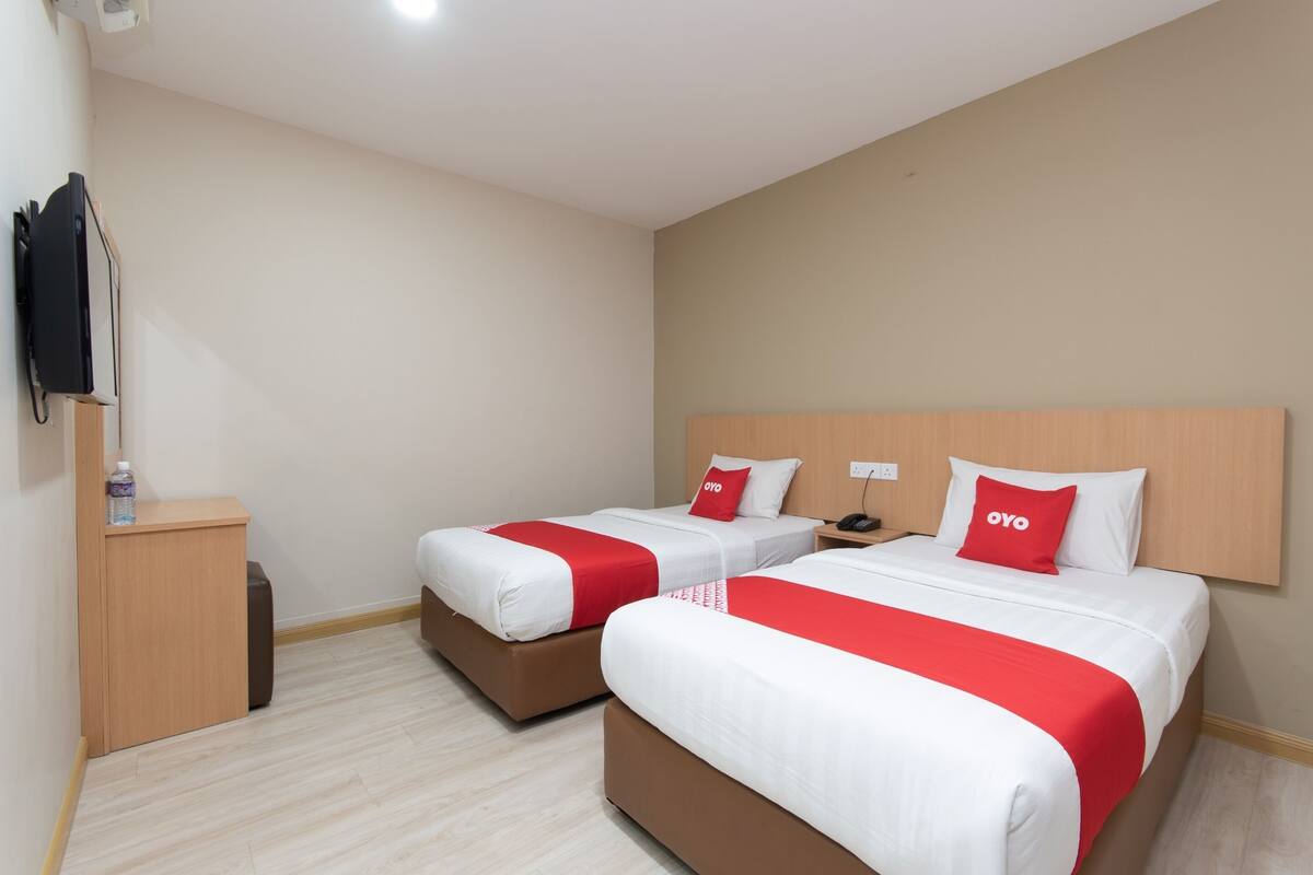 A hotel room with two beds, each with red and white bedding, a wooden headboard, and a small bedside table with a lamp.