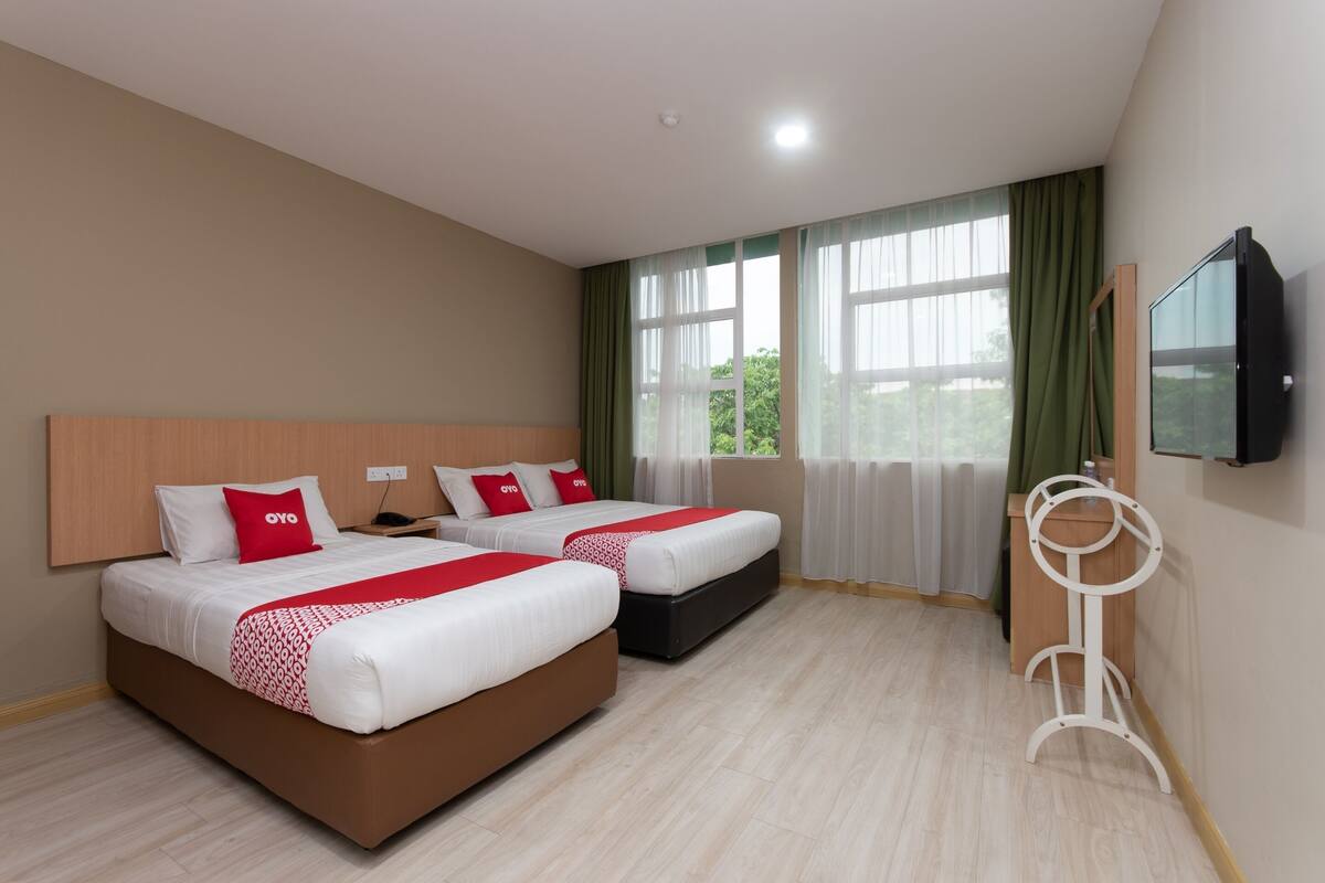 A hotel room with two beds, a TV, and a window with curtains.