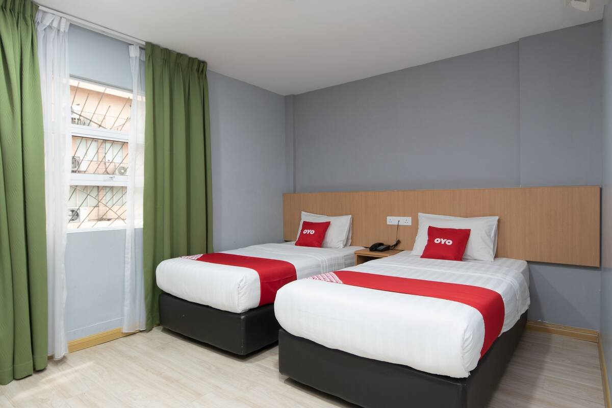 A hotel room with two beds, green curtains, a window with a view, and a wooden headboard.