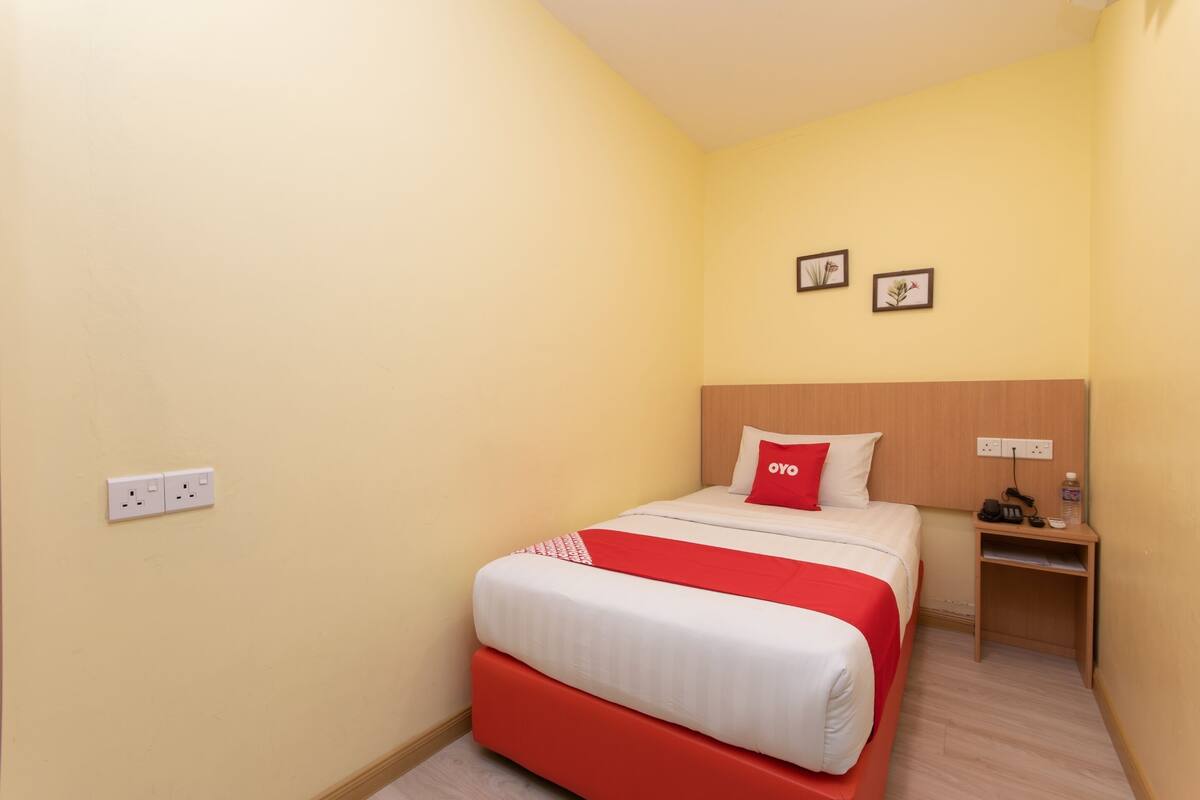 A hotel room with a bed, a nightstand, and two framed pictures on the wall.