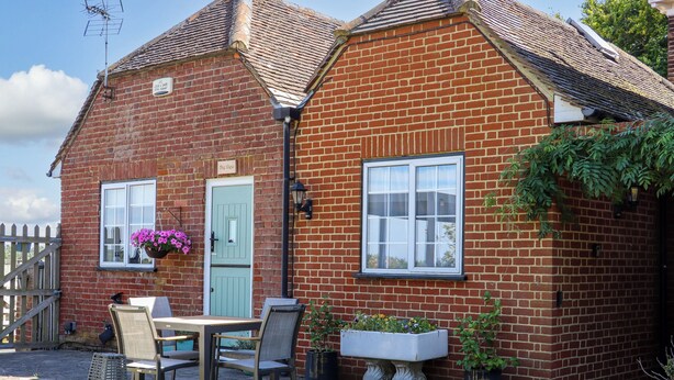 A brick house with a green door, a window with a hanging flower basket, and a table with chairs outside. - The View (Faversham)