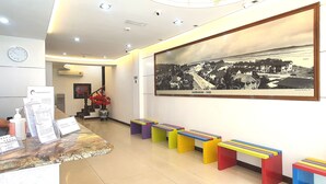 Una zona de recepción con mostrador de mármol, asientos coloridos, una fotografía grande en blanco y negro enmarcada y un reloj en la pared.