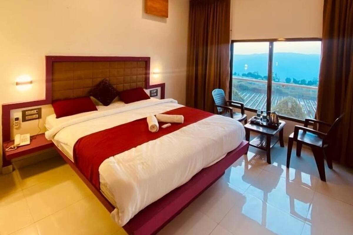 A hotel room with a large bed, a desk, and a view of the landscape.