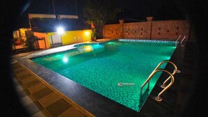 A swimming pool at night with a ladder and a tiled deck. - Hollywood Palace Resort (Mahabaleshwar)