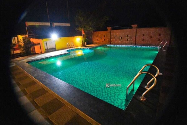 A swimming pool at night with a ladder and a tiled deck. - Hollywood Palace Resort (Mahabaleshwar)