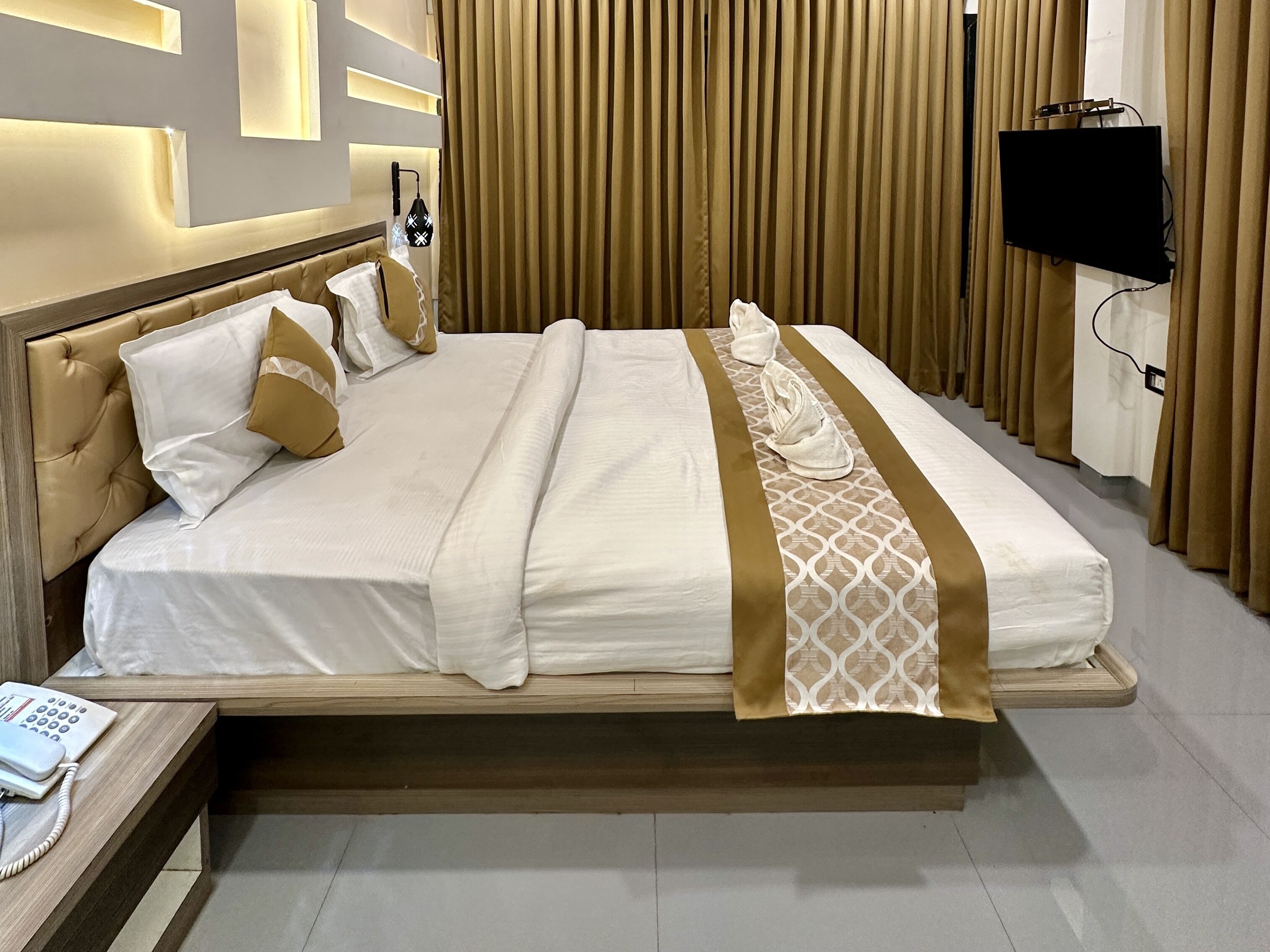 A hotel room with a large bed, a bedside telephone, and a television mounted on the wall.