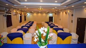 A conference room with rows of chairs, a central table with a blue tablecloth, and a potted plant with white flowers. - Hollywood Palace Resort (Mahabaleshwar)