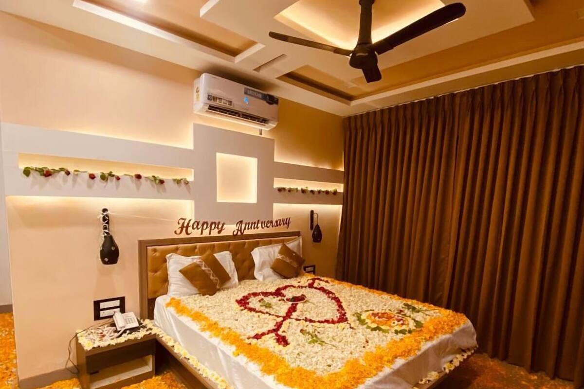 A bedroom with a bed, a ceiling fan, an air conditioning unit, and a 'Happy Anniversary' sign.
