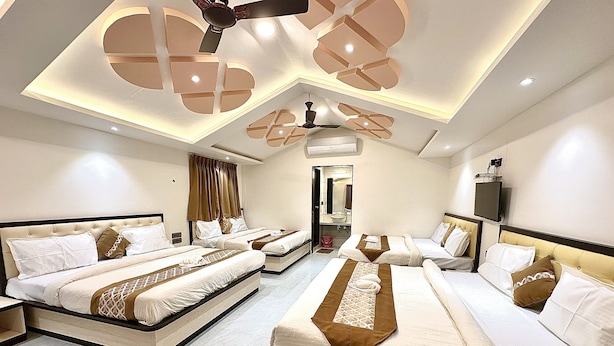 A hotel room with two large beds, a ceiling fan, a TV, and a bathroom visible through an open door. - Hollywood Palace Resort (Mahabaleshwar)