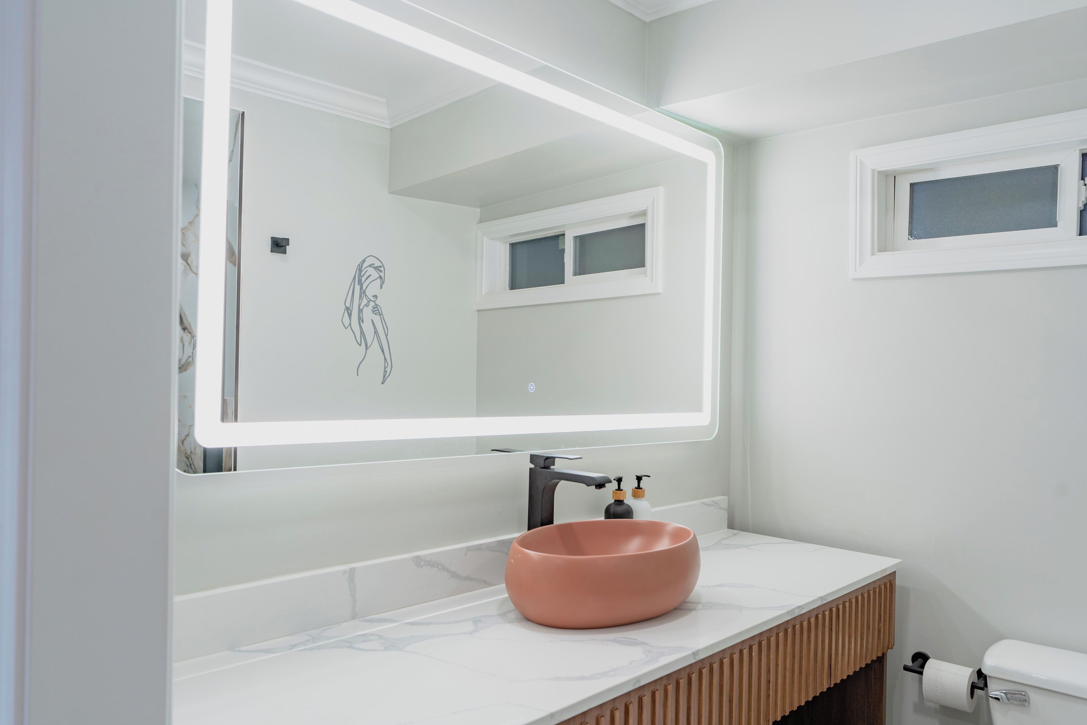 Un baño moderno con un espejo grande, un lavamanos redondo y un inodoro.