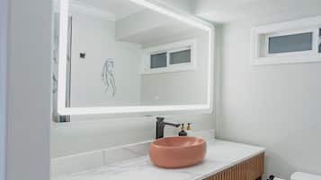 Un baño moderno con un espejo grande, un lavamanos redondo y un inodoro.