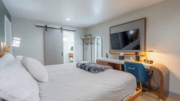 A modern hotel room with a large bed, a desk with a computer, a TV, and a wardrobe.