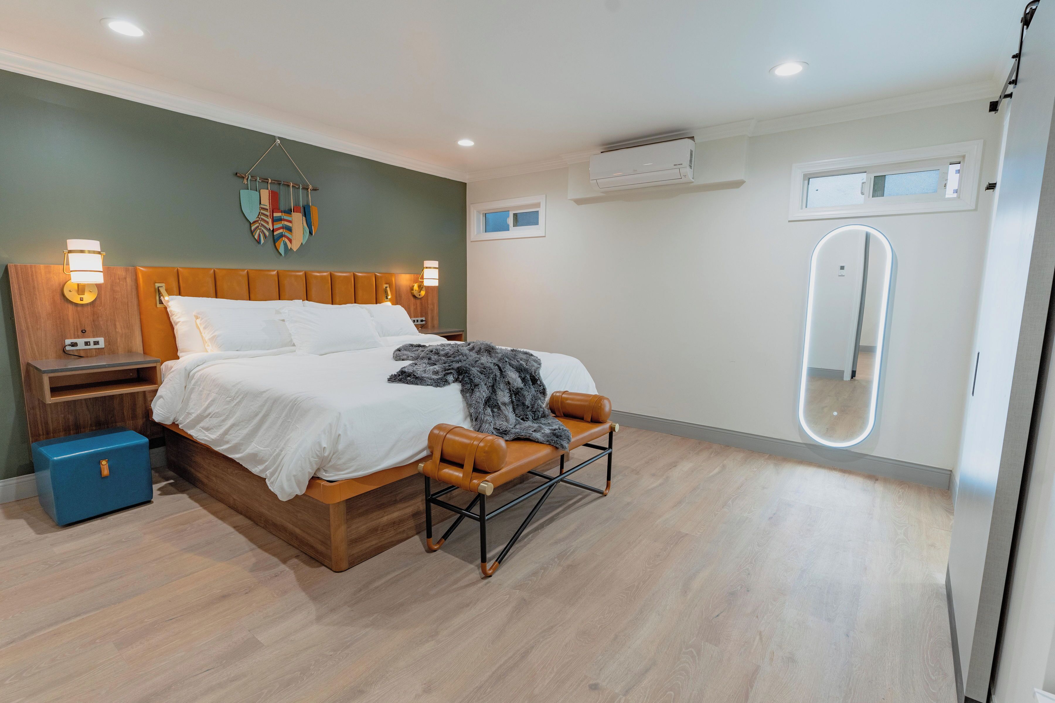 Une chambre à coucher moderne avec un lit en bois, des tables de chevet, un banc et un grand miroir.