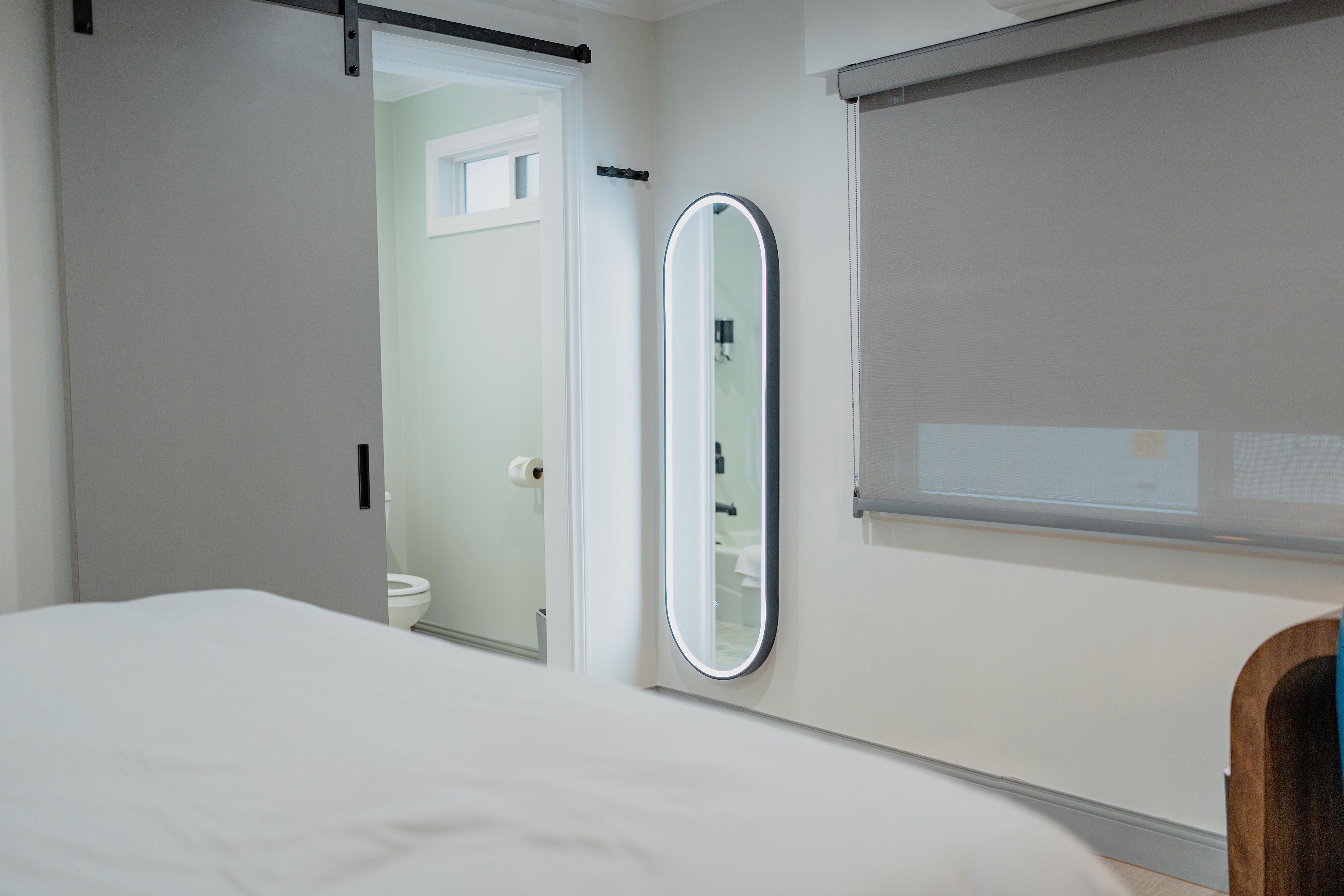 Una habitación de hotel moderna con una cama grande, un baño con inodoro y espejo, y una ventana con persianas.