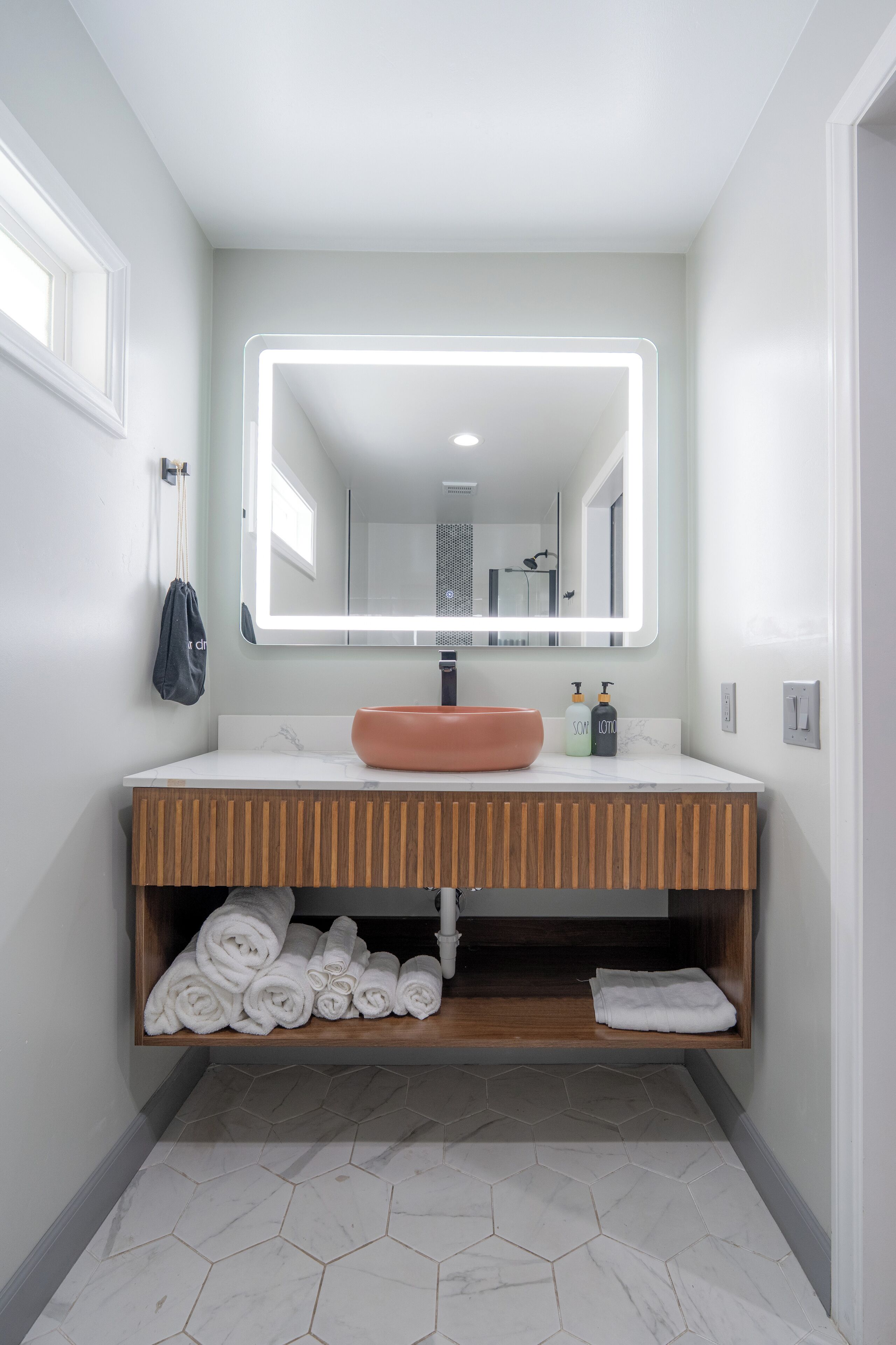 Uma casa de banho moderna com toucador branco, um espelho grande e pavimento em azulejos hexagonais.