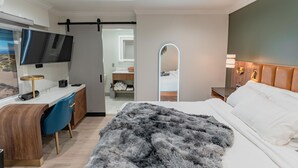 Un dormitorio moderno con una cama, un escritorio, un televisor y un espejo.