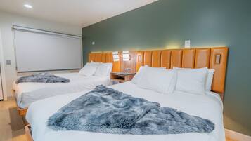 Camera d'albergo con due letti, entrambi con lenzuola bianche e una coperta azzurra soffice. La stanza ha una testiera in legno e un'ampia finestra con tende.