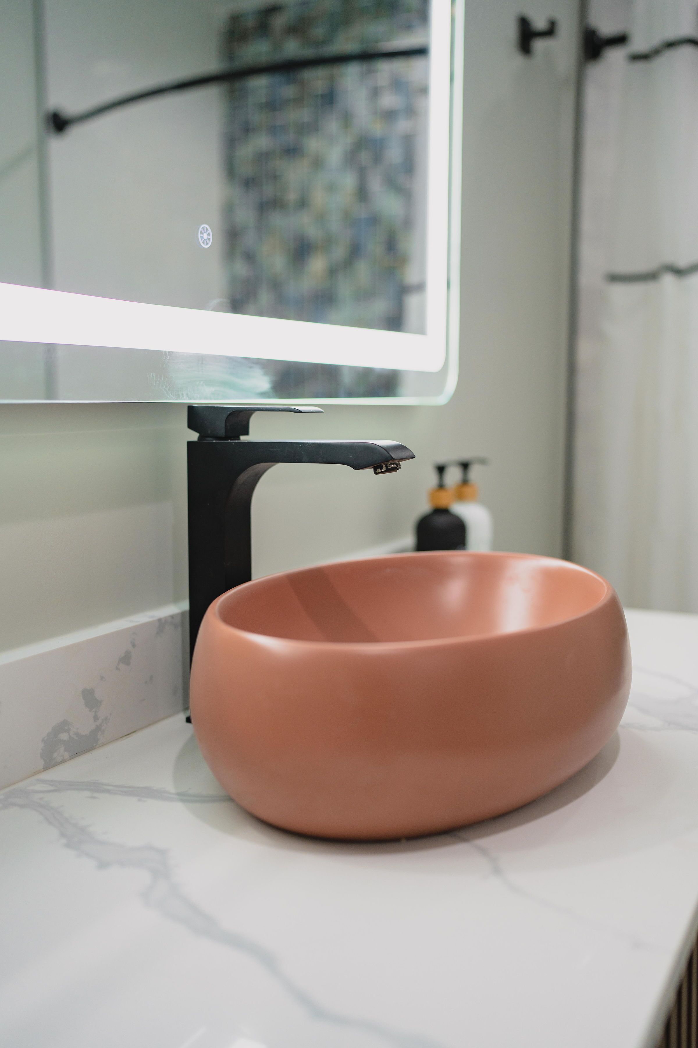 A bathroom with a round, terracotta-colored sink mounted on a white marble countertop.