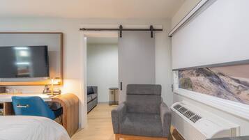 Ein Hotelzimmer mit Bett, Schreibtisch mit Computer, Stuhl, Fernseher, Fenster mit Aussicht und Klimaanlage.