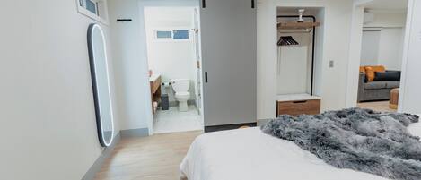 Un dormitorio moderno con una cama grande, un vestidor y un baño visible a través de una puerta abierta.