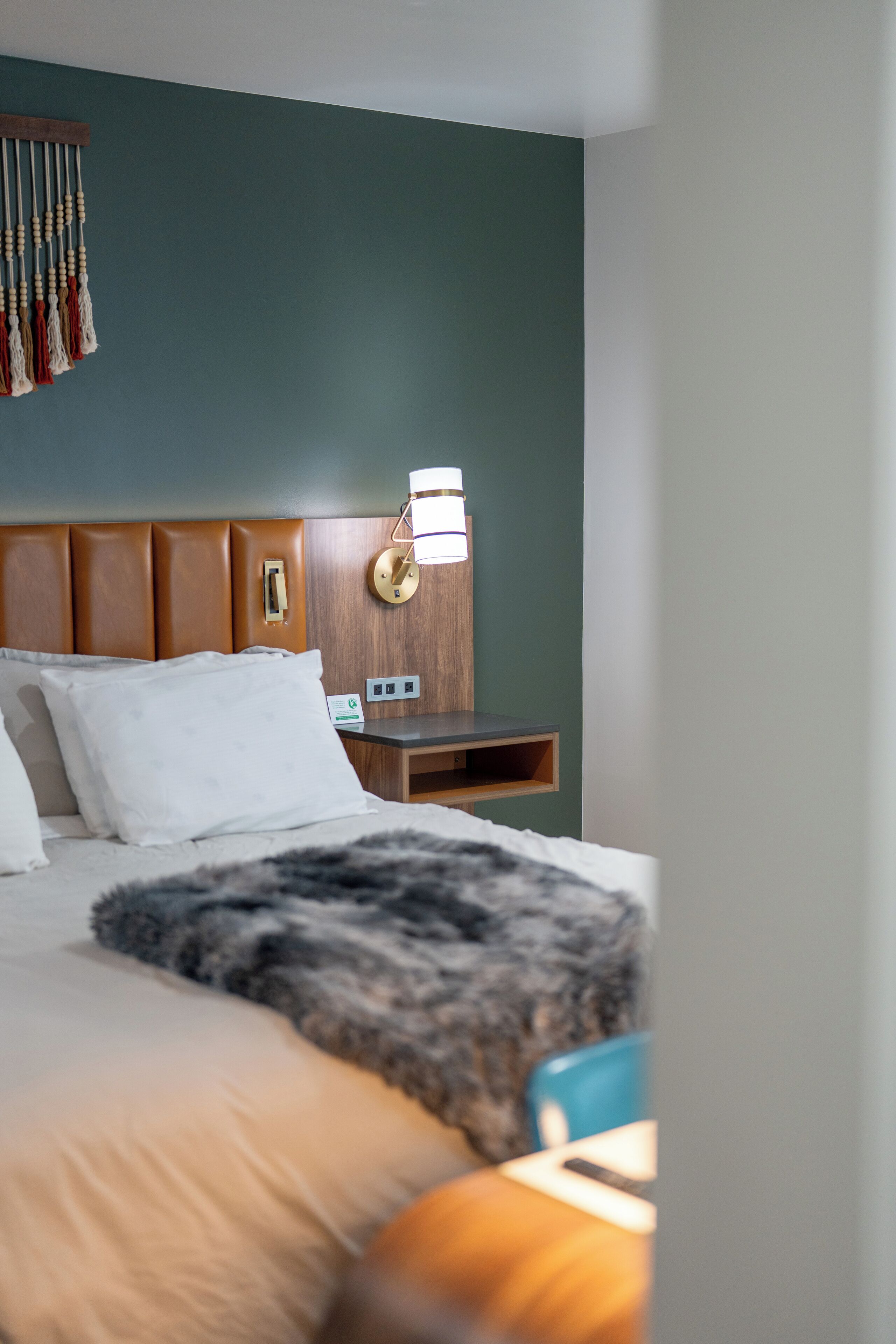 Una cama bien hecha con un edredón mullido, un cabecero de madera, una mesita de noche con una lámpara y una lámpara de pared.