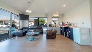 Amplia sala de estar con sofá, sillones, una mesa de centro y una zona de cocina con refrigerador y armarios.