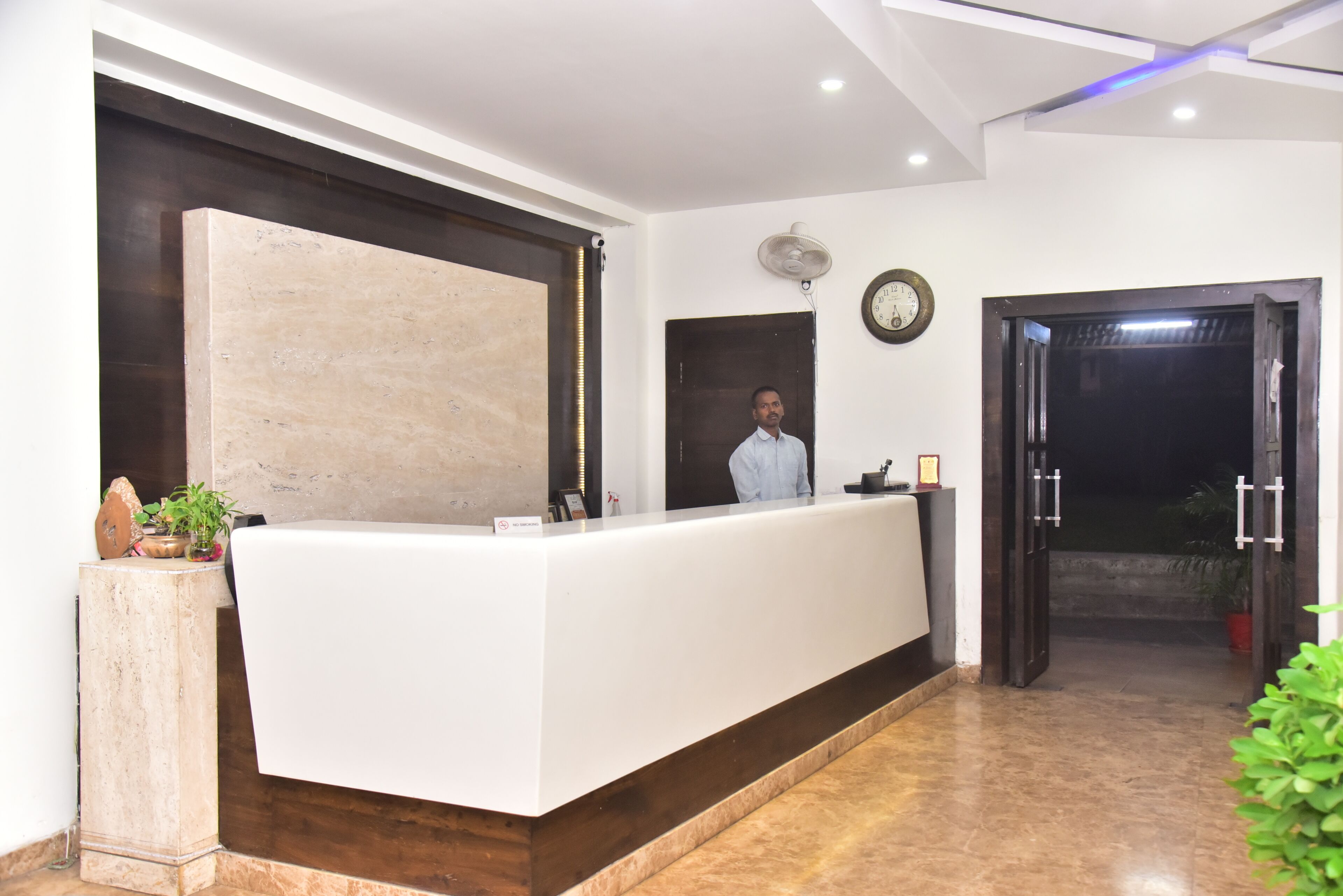 A reception desk with a clock, a fan, and a door leading to another room.