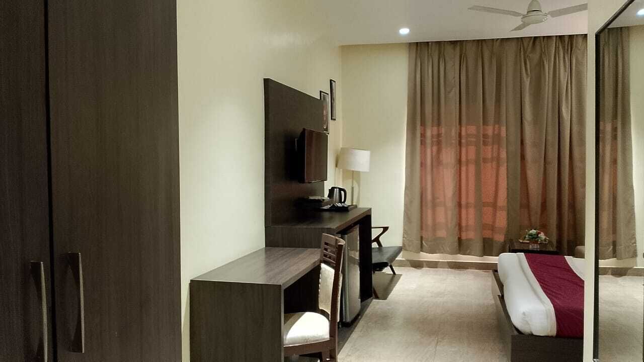 A hotel room with a bed, a desk with a chair, a television, a lamp, and a window with curtains.