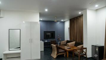 A modern living room with a dining area, a flat-screen TV, and a ceiling fan.