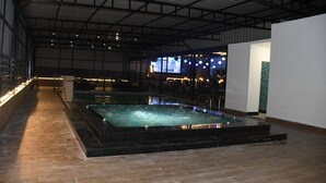 An indoor swimming pool with a tiled floor, surrounded by walls and a high ceiling. - VEENA REGENCY (Chas)